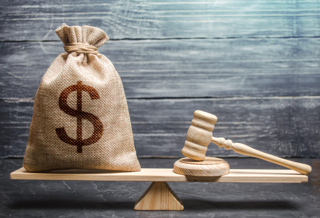 Sack of money on a wooden scale with a gavel on the opposite side.