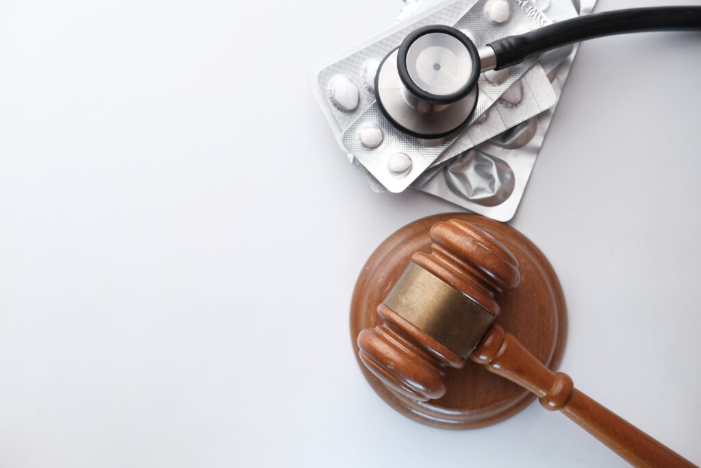 A gavel representing healthcare law placed beside a stethoscope and a blister packs of pills.