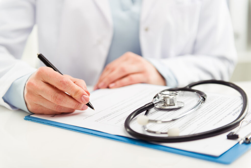 Young woman physician wearing a stethoscope, writing a prescription.
