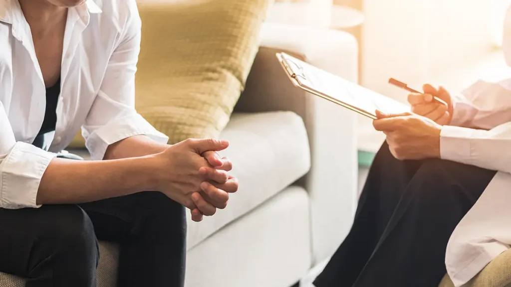 A female patient is sitting down with a mental health professional, presumably receiving therapy. Healthcare fraud concept.